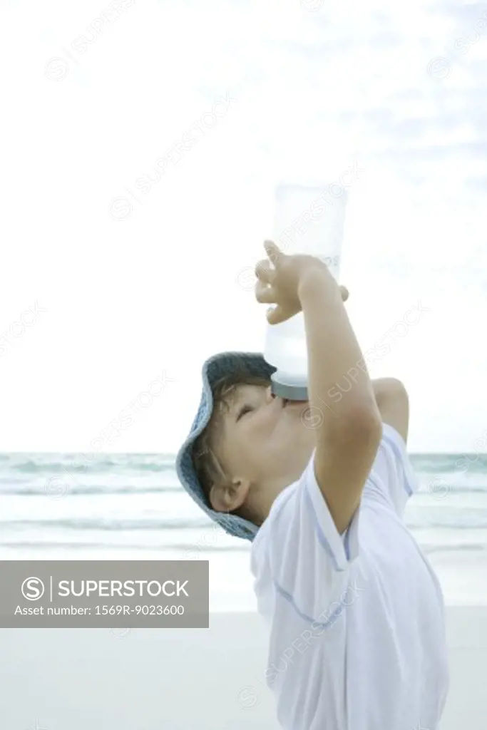 Boy drinking from water bottle on beach