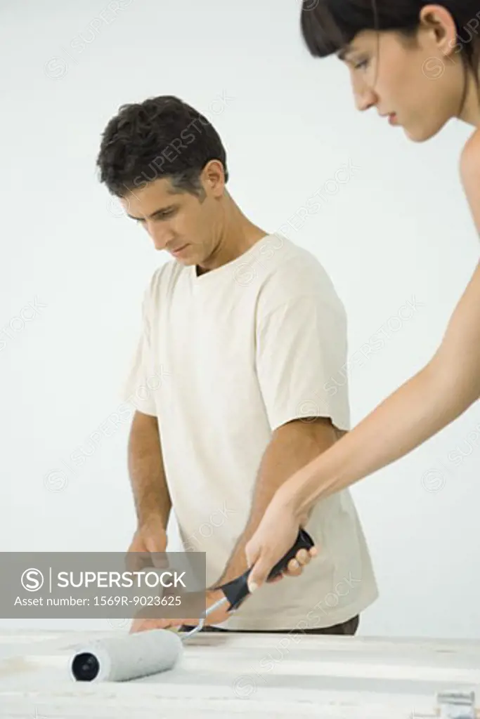 Woman painting door while man applies masking tape