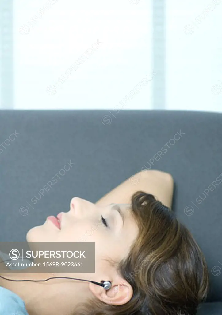 Young woman lying on couch, listening to earphones