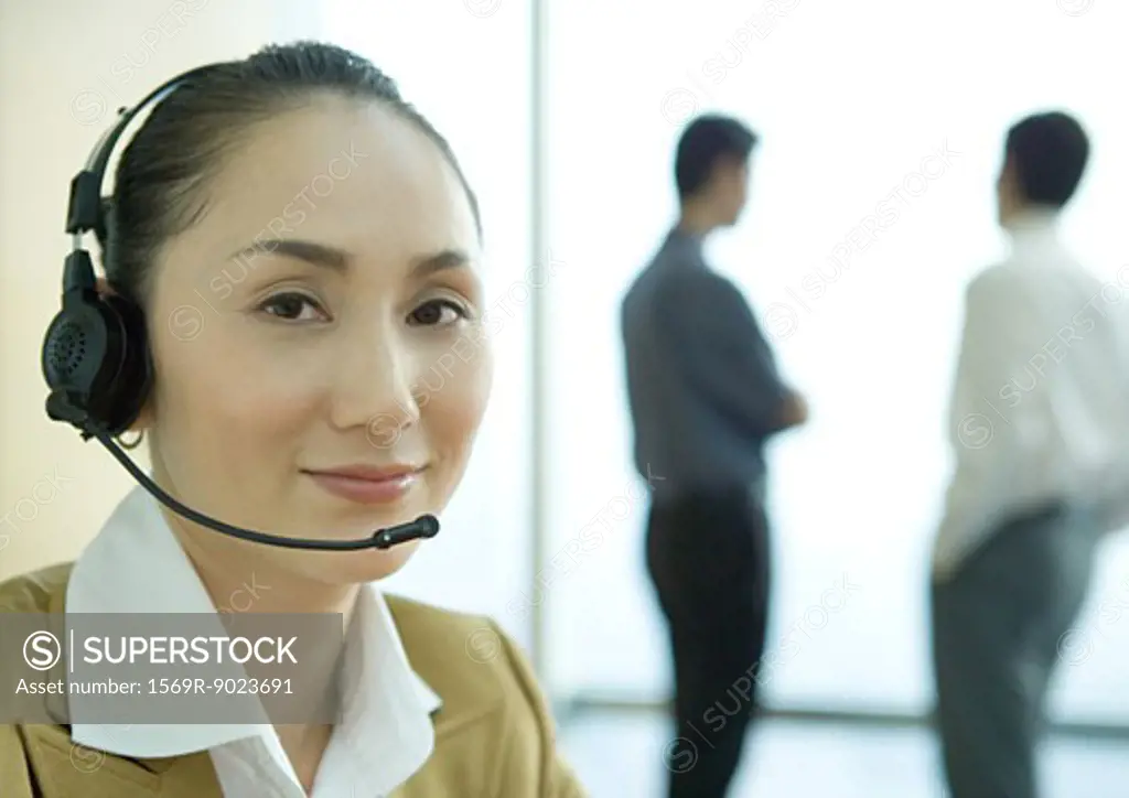 Businesswoman wearing headset, colleagues standing in background, portrait