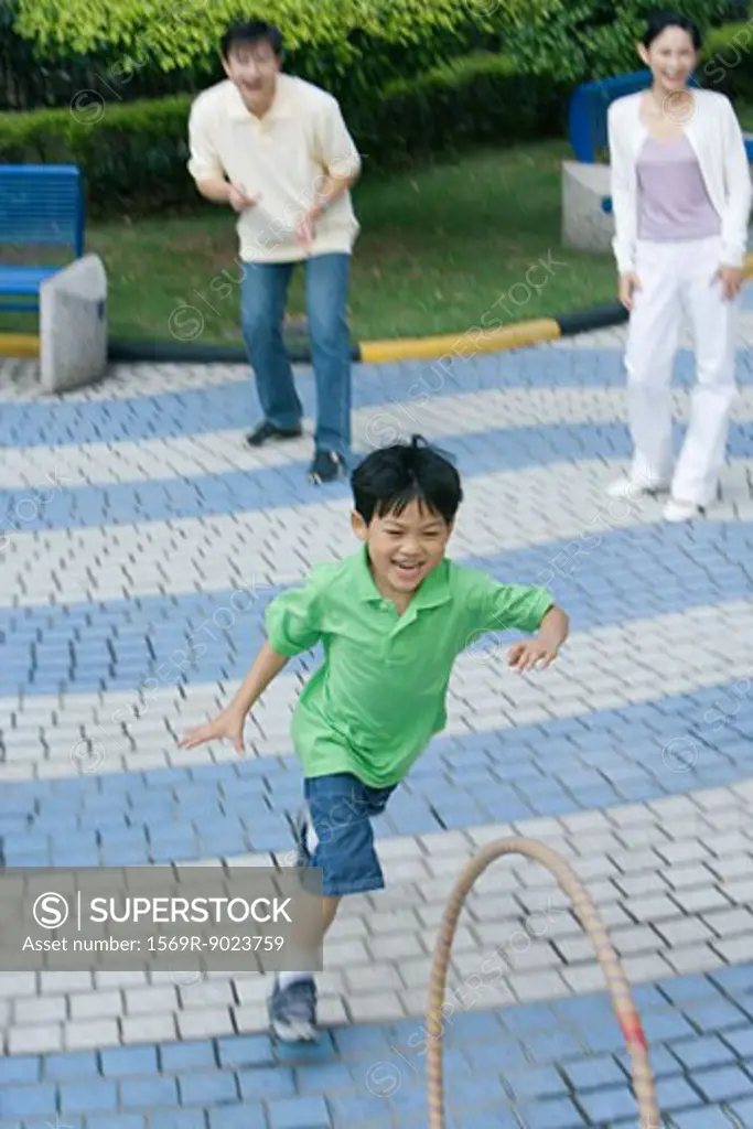 Boy chasing hoop, parents watching