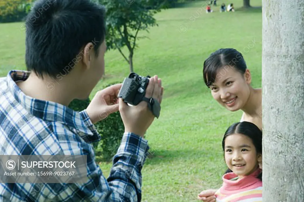 Man filming wife and daughter in park with video camera
