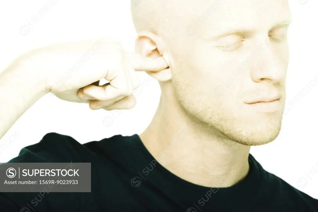 Young man plugging ear with finger, eyes closed