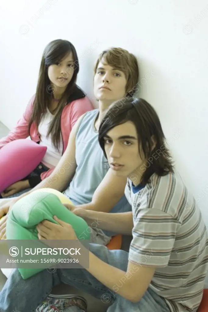 Three teen friends sitting on floor, holding cushions