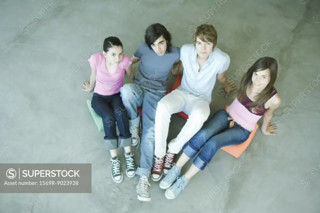 Four teen friends sitting on cushions on ground, looking at camera, high angle view