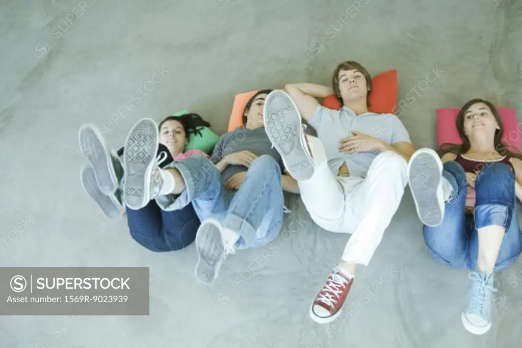 Four teen friends lying on backs on floor, holding up legs, focus on soles of shoes