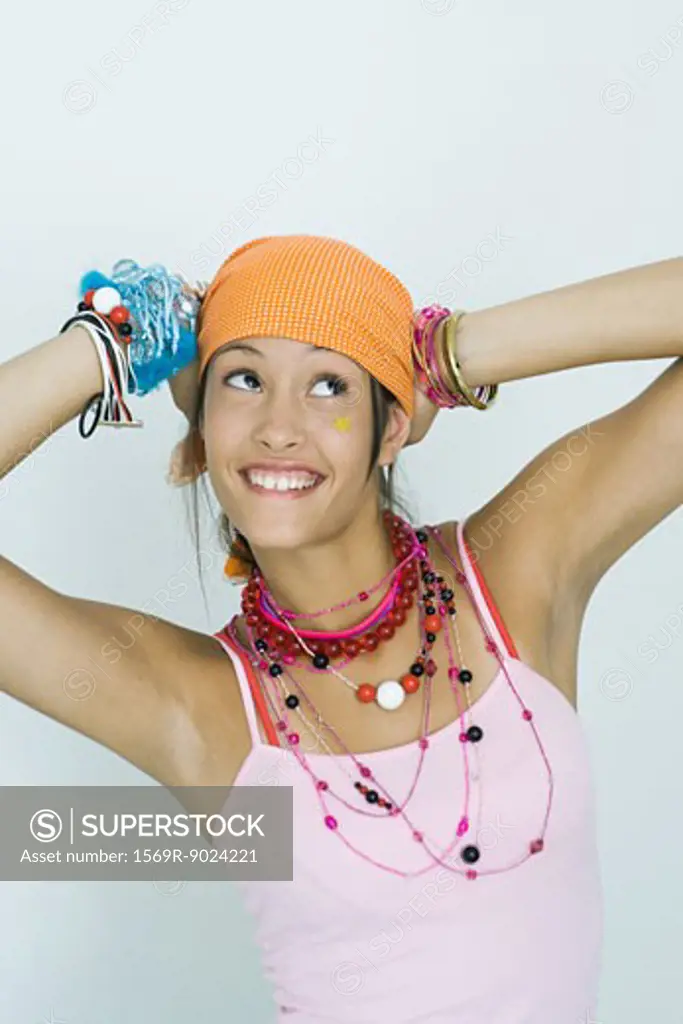 Teenage girl wearing lots of jewelry, hands behind head, looking up, smiling, portrait