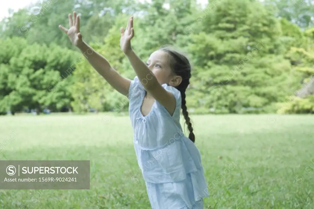 Girl standing on grass with arms in air