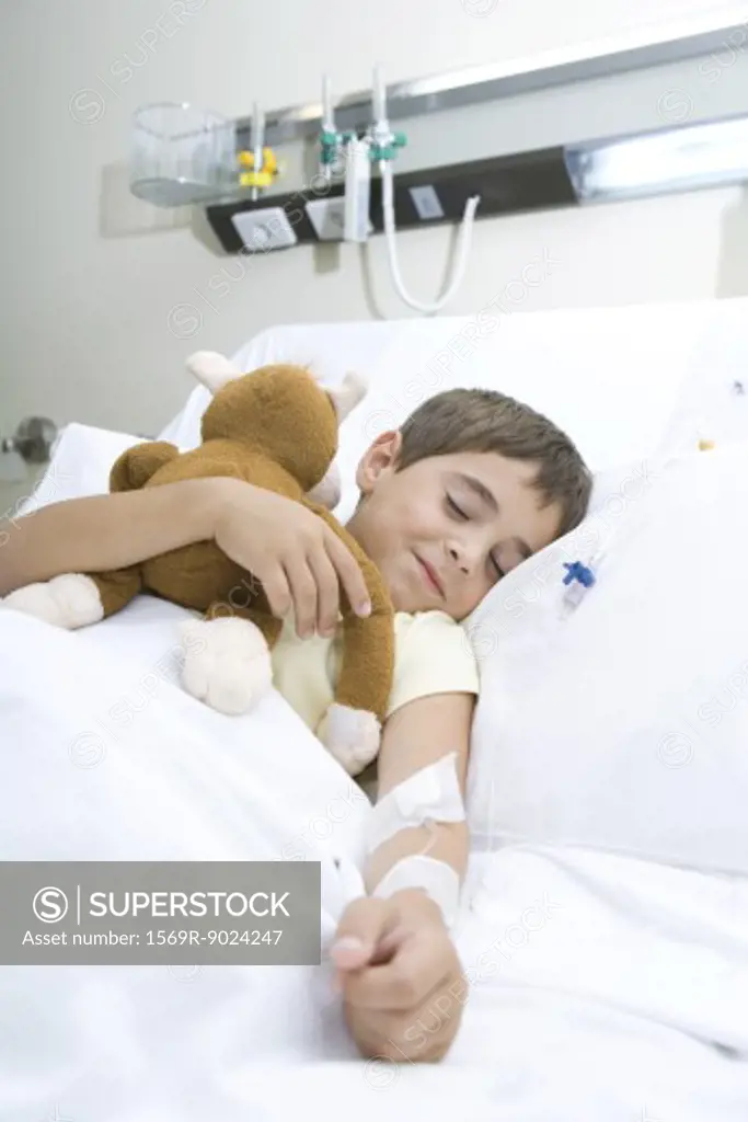 Boy sleeping in hospital bed sleeping, holding stuffed animal, smiling