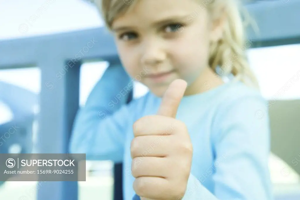 Girl giving camera thumbs up sign, focus on hand in foreground