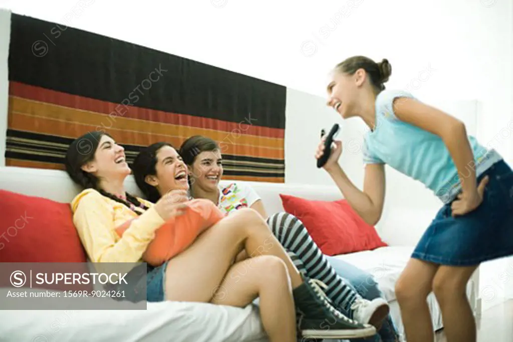 Preteen girl singing into remote control, friends laughing