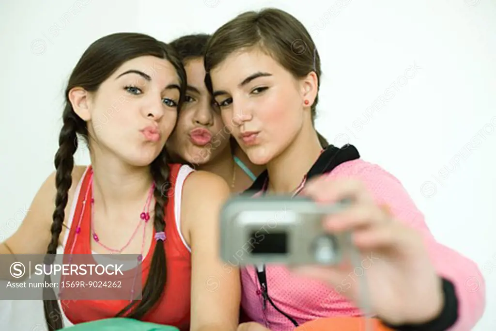 Three young female friends puckering as one takes photo with digital camera