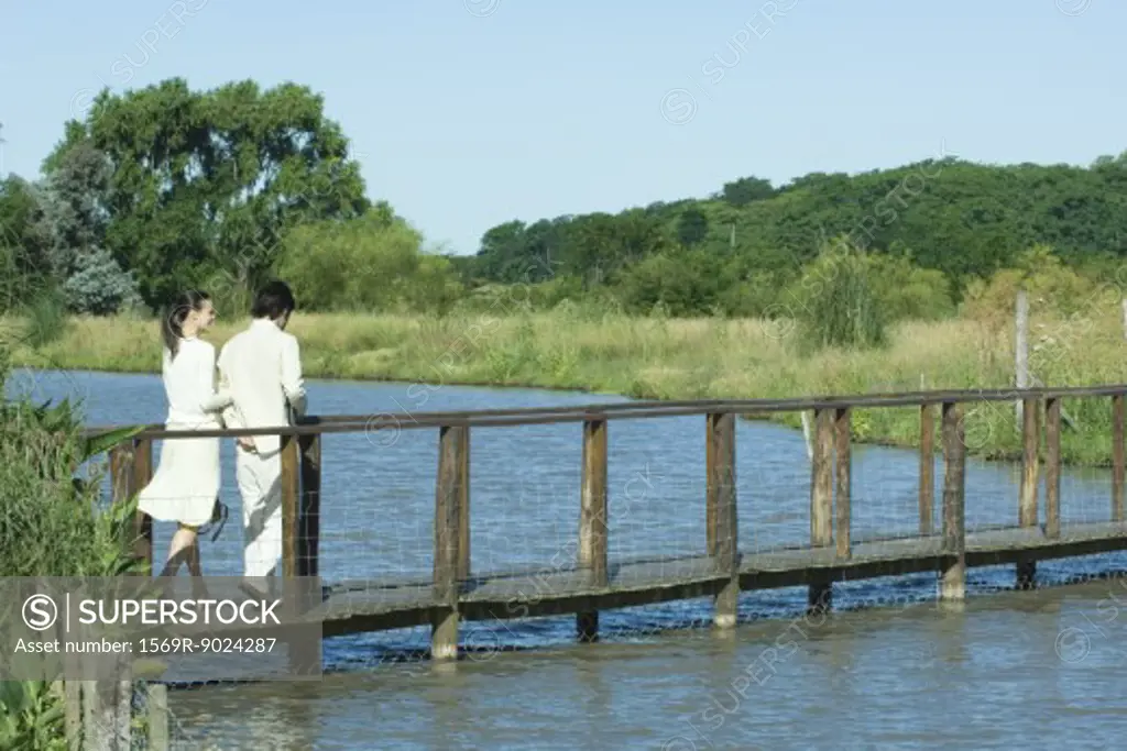 Couple walking over river on footbridge