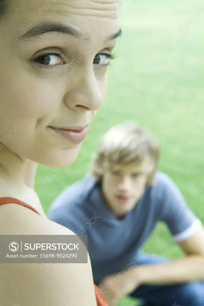 Teen girl looking over shoulder at camera, raising eyebrows, male friend in background