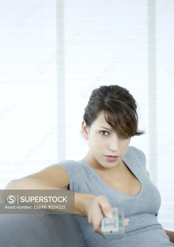Young woman pointing remote control, looking at camera