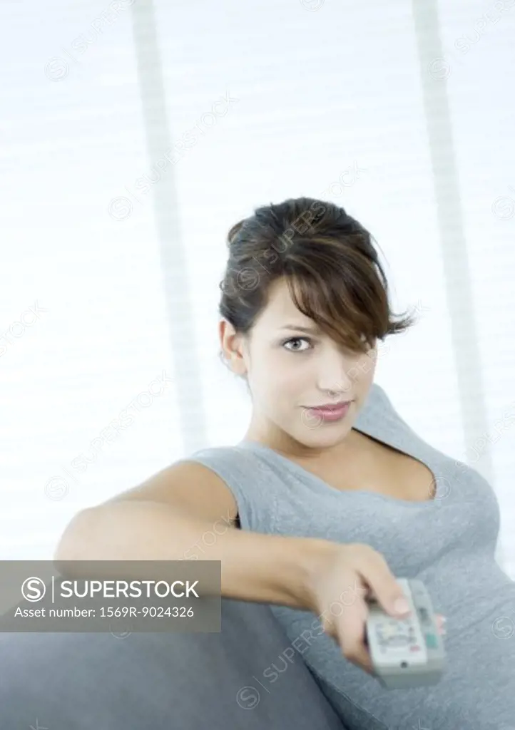 Young woman pointing remote control, smiling at camera