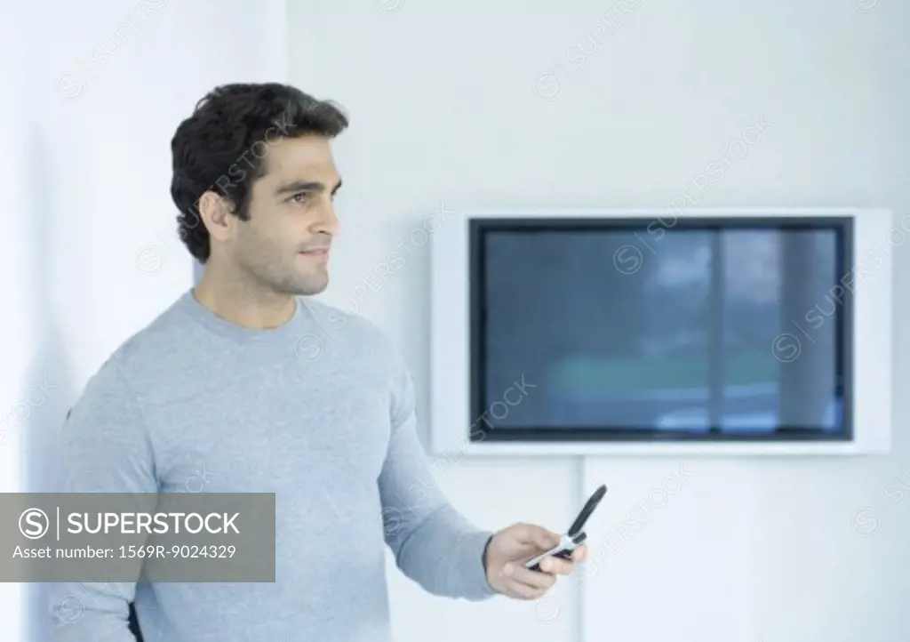 Man holding out cell phone, looking away, widescreen TV in background