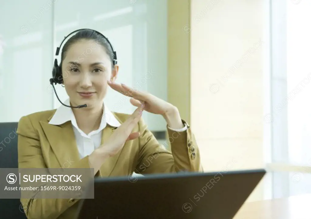 Businesswoman wearing headset and using laptop, making time out gesture