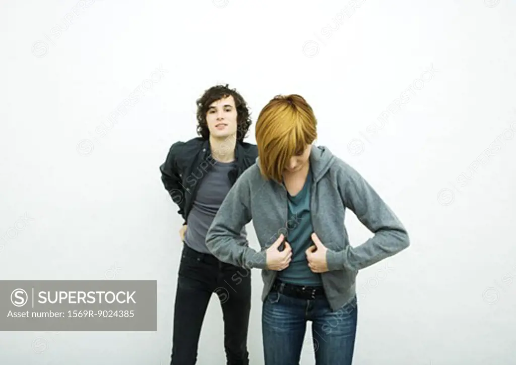 Two young adults putting on jackets, white background