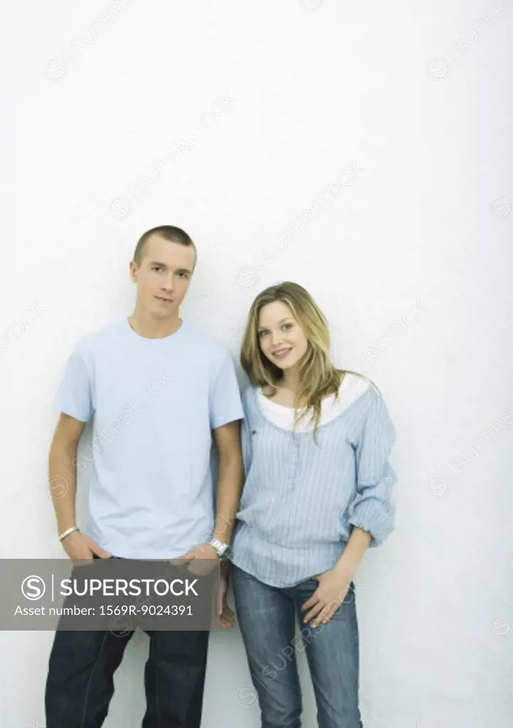 Young couple standing side by side, looking at camera, portrait, white background