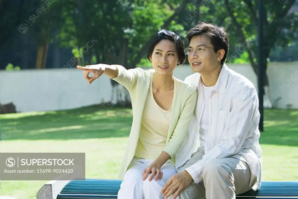 Couple sitting on bench, woman pointing out of frame