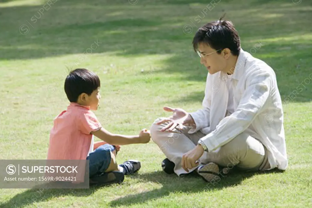 Father and son sitting on grass playing "rock paper scissors"