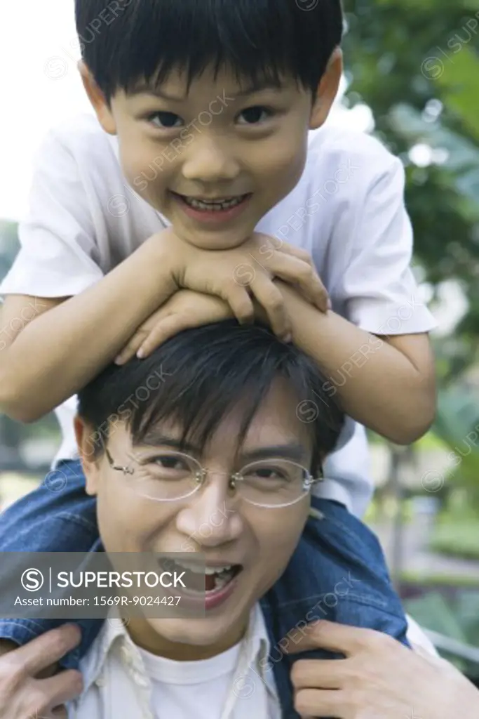 Boy riding on father's shoulders, front view, smiling at camera