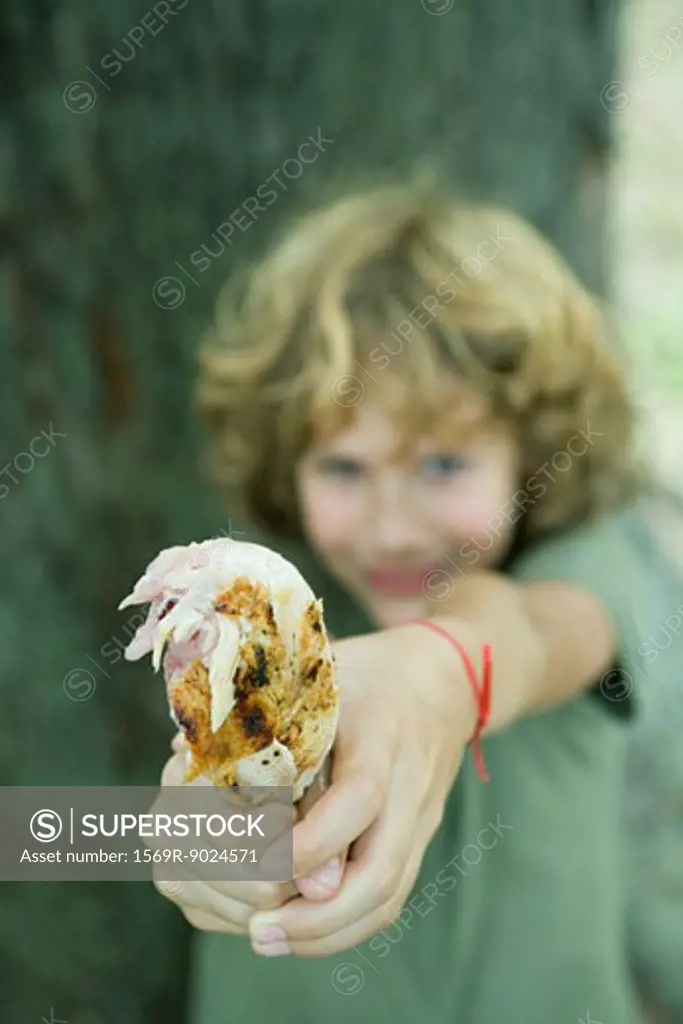 Boy holding out grilled chicken leg