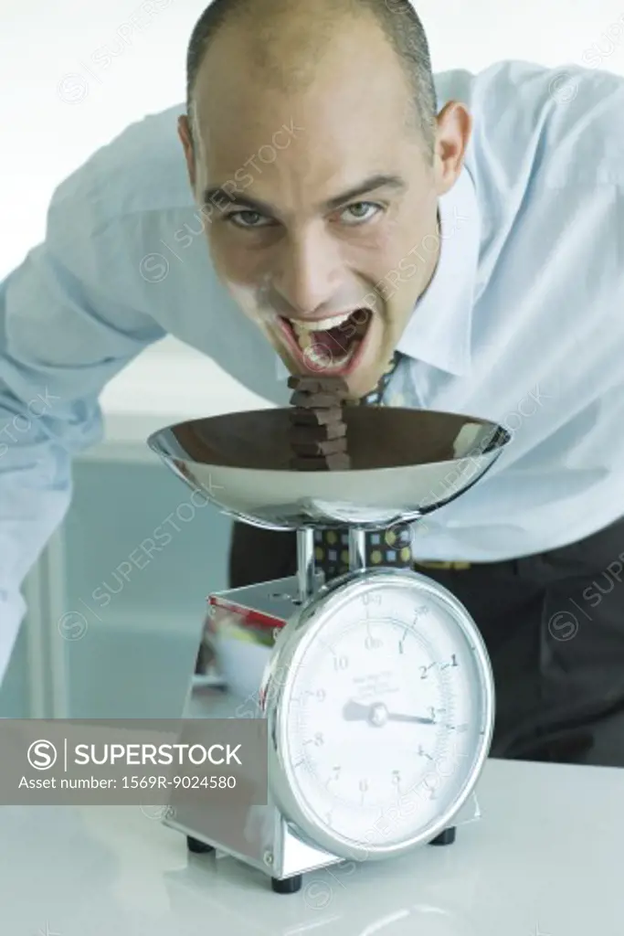 Man leaning toward stack of chocolate chunks on kitchen scale with mouth wide open