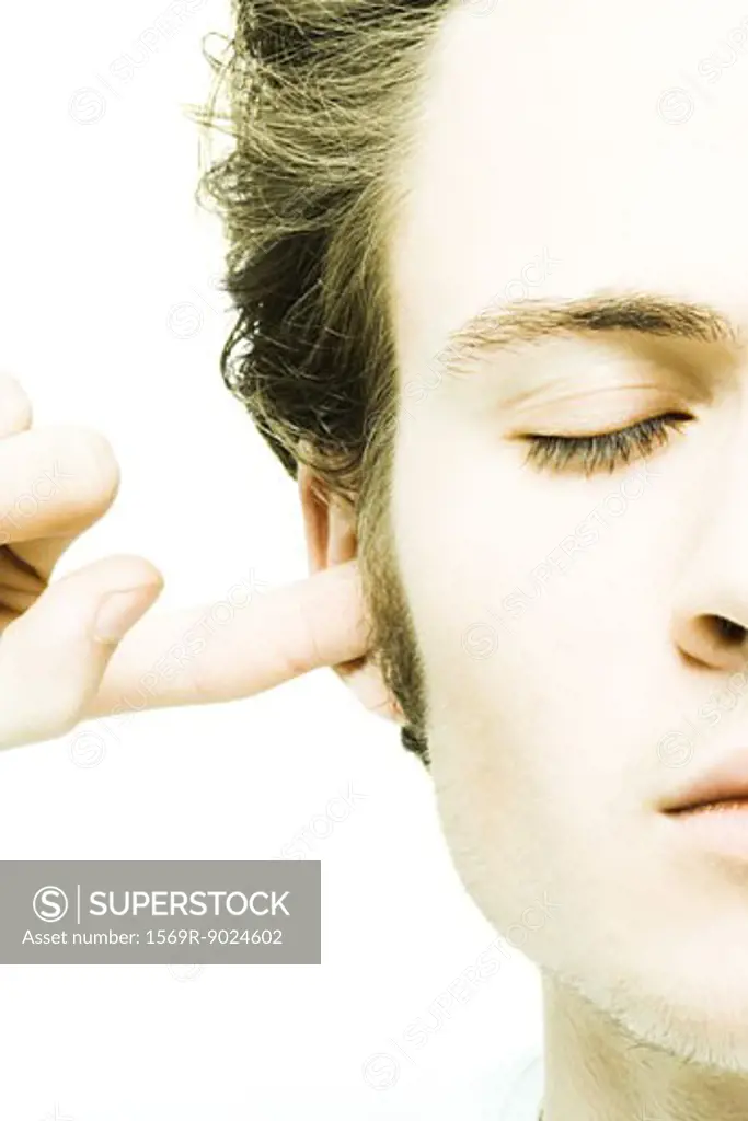 Young man plugging ear, eyes closed