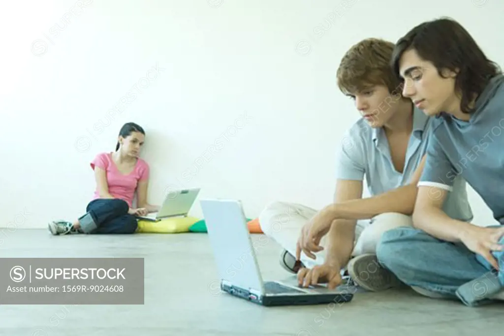 Teens sitting on floor, using laptops