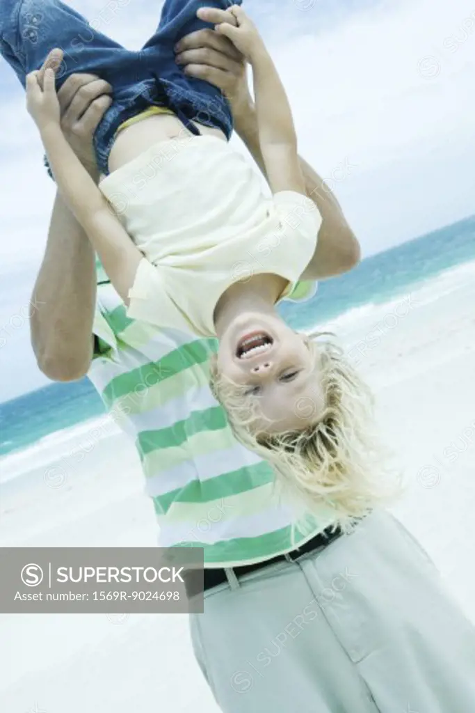 Man holding child upside down on beach