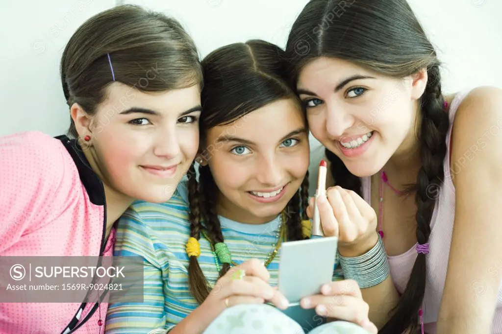 Three young female friends holding make-up, smiling at camera