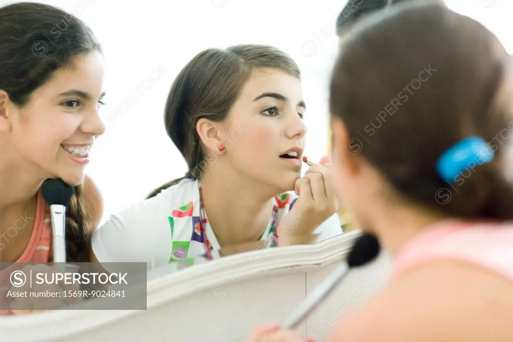 Young female friends looking at mirror, putting on make-up