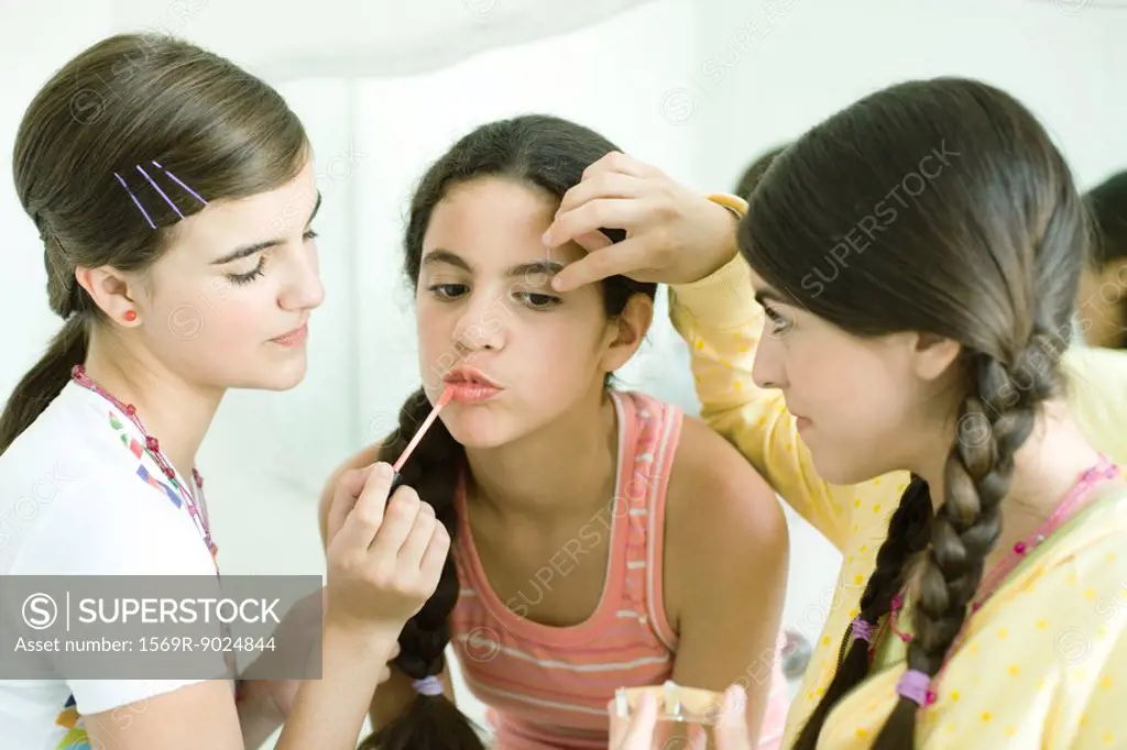 Two young female friends putting make-up on younger girl
