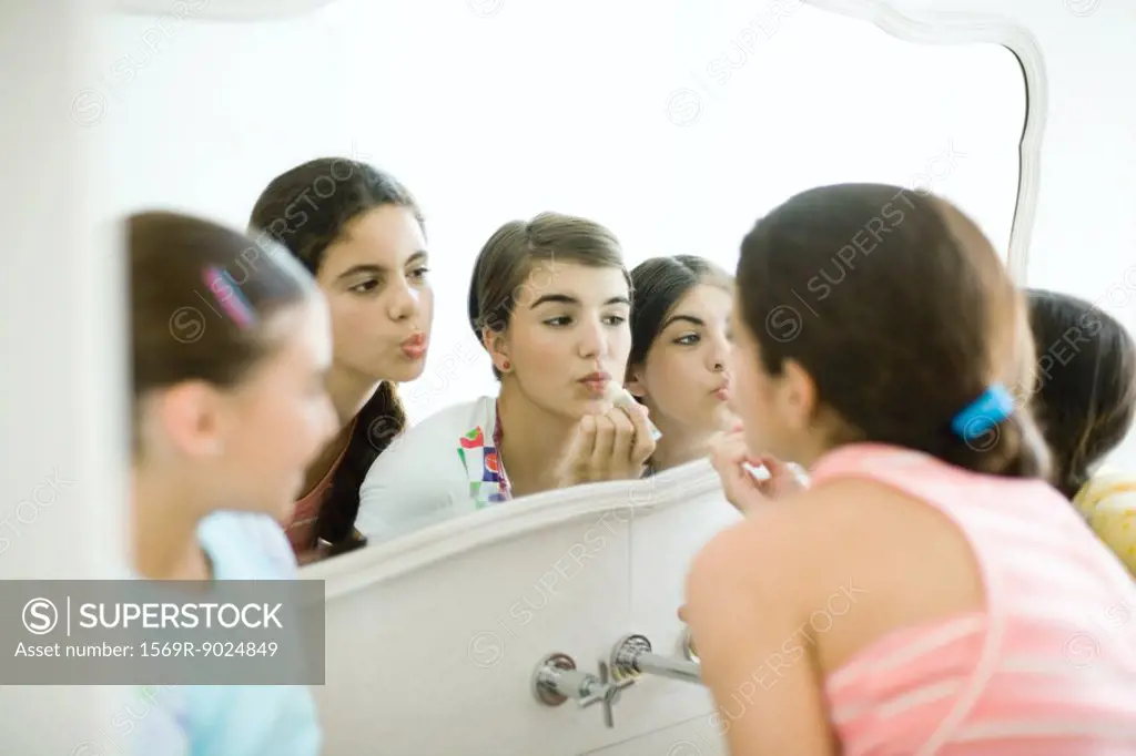 Young female friends looking at mirror, putting on make-up