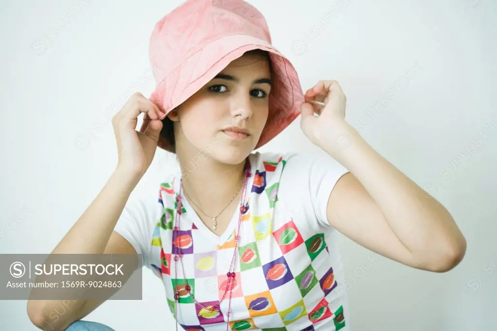 Teen girl putting on hat, portrait