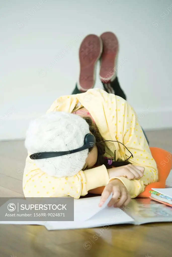 Young woman lying on floor listening to headphones, head on arm
