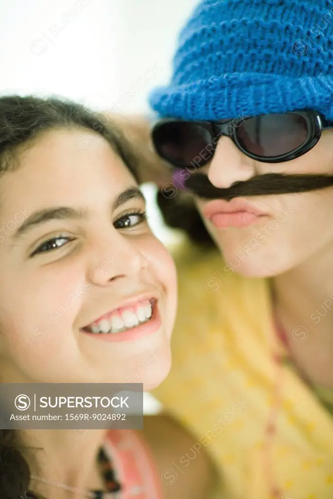 Two young female friends, one holding hair below nose like mustache, portrait