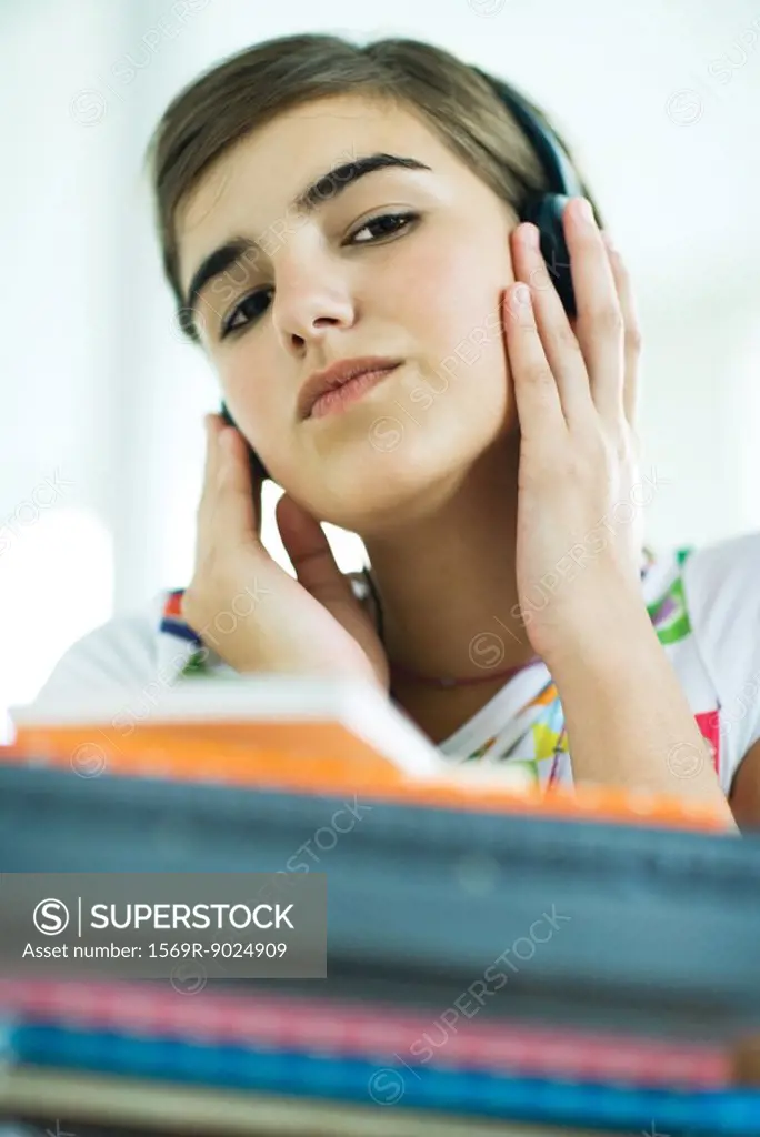 Teen girl with stack of homework, listening to headphones, portrait