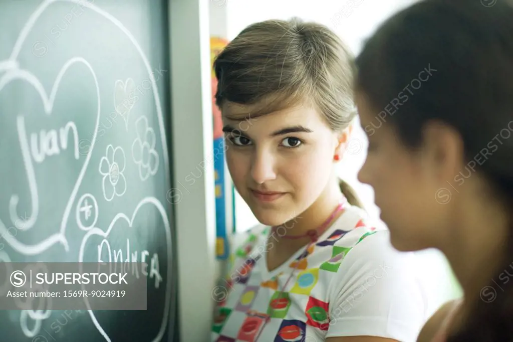 Young female friends writing names in hearts on chalkboard