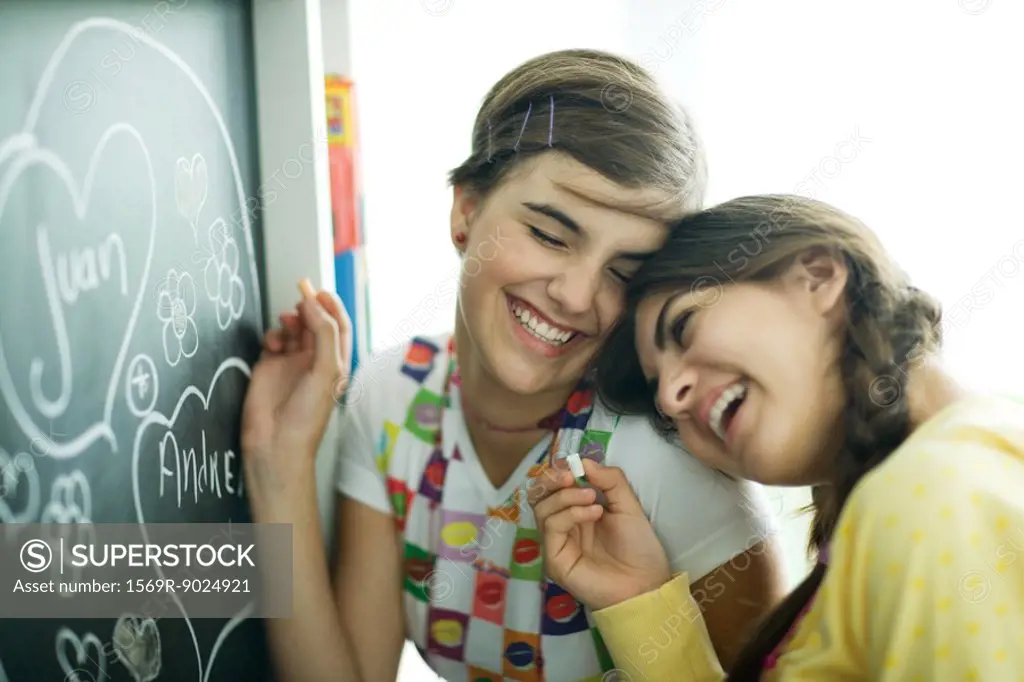 Young female friends writing names in hearts on chalkboard, laughing