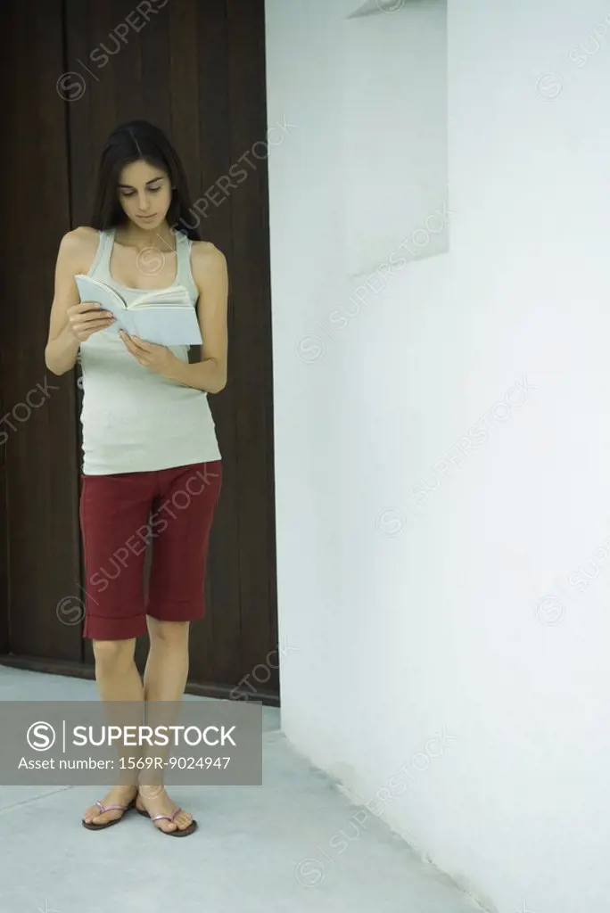 Woman standing reading book, full length portrait
