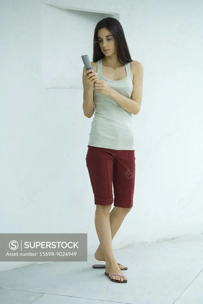 Woman standing dialing cell phone, full length portrait