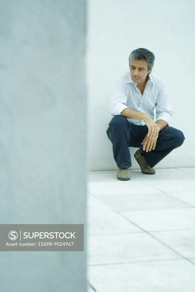 Mature man crouching, looking down, full length portrait