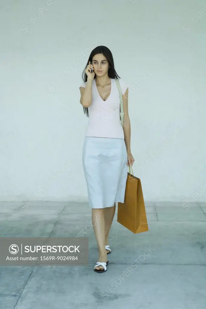 Woman carrying shopping bags, using cell phone, full length portrait