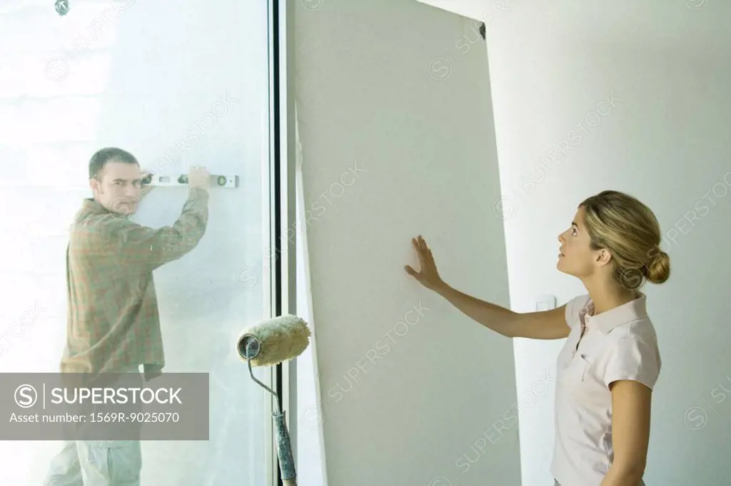 Man holding level against wall and woman putting hand against wall board