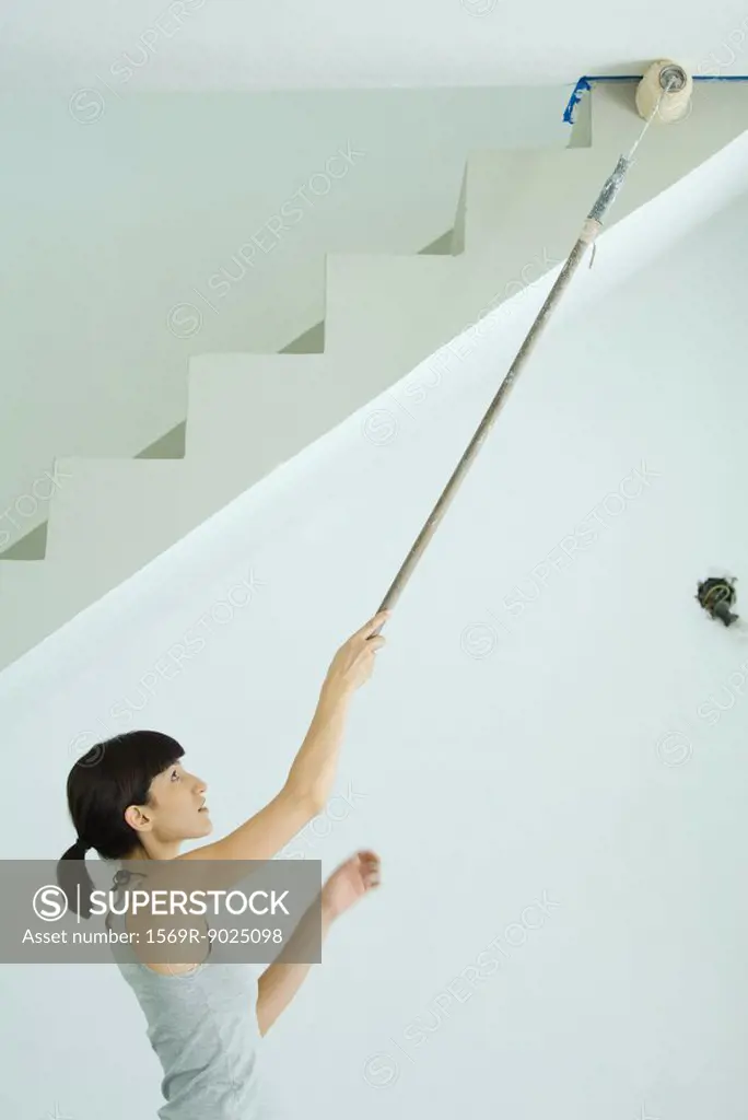 Woman painting ceiling with roller extension