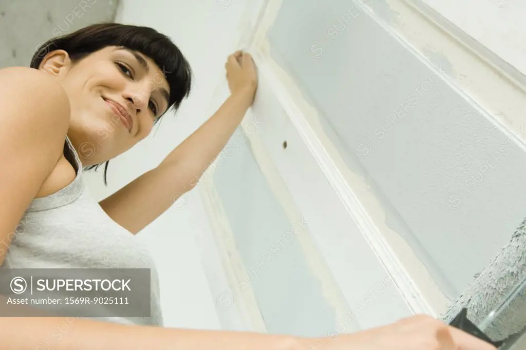 Woman painting door with paint roller, smiling at camera, low angle view