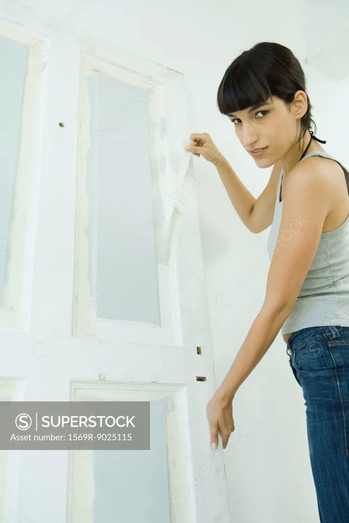 Woman removing masking tape from freshly painted woodwork on door